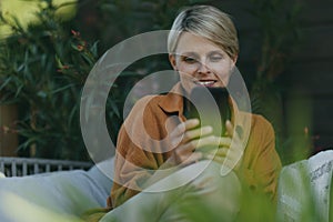 Beautiful woman relaxing in the garden, scrolling on smartphone. Mother having a moment to herself while her child is