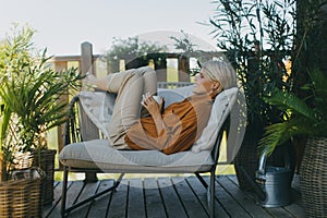 Beautiful woman relaxing in the garden, sitting on patio chair and drinking cup of coffee. Mother having moment to