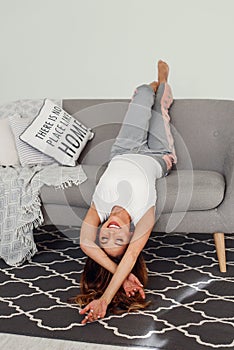 Beautiful woman relaxing on a grey couch with head upside down. Cute girl having fun at cozy home in lazy day. photo