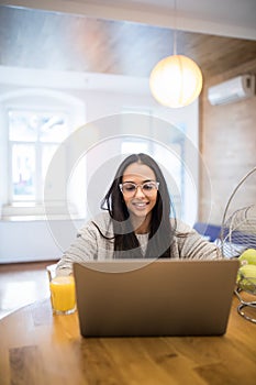 Beautiful woman relaxing with her laptop with glass of orange juice in the kitchen