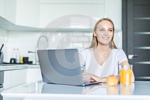 Beautiful woman relaxing with her laptop while holding glass of orange juice in the kitchen