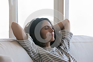 Beautiful woman relaxing on sofa with hands behind head, closeup