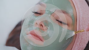 beautiful woman relaxing in spa salon, closeup of face with clay mask, cosmetologist applying mud