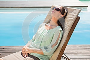 Beautiful woman relaxing on sun lounger by swimming pool