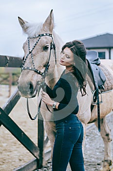 A beautiful woman rider talks to her horse after riding in a country ranch. Lifestyle Photo. Fashion photo.