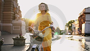 Beautiful woman riding a city bicycle with a basket and flowers in the city center during the dawn enjoying her time