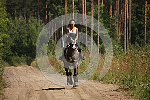 Beautiful woman riding gray horse in the forest