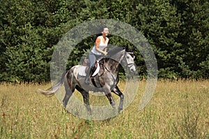 Beautiful woman riding gray horse in the forest