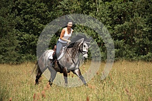 Beautiful woman riding gray horse in the forest