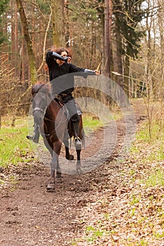 Beautiful woman riding in historical costume as a warrior rides a horse and shoots an arrow from a bow