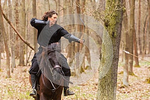 Beautiful woman riding in historical costume as a warrior rides a horse and shoots an arrow from a bow