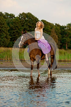 Beautiful woman riding a horse at sunset on the beach. Young beauty girl with a horse in the rays of the sun by the sea