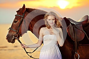 Beautiful woman riding a horse at sunset on the beach. Young girl with a horse in the rays of the sun by the sea.