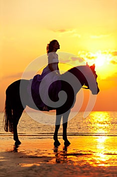 Beautiful woman riding a horse at sunset on the beach. Young girl with a horse in the rays of the sun by the sea.