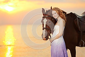 Beautiful woman riding a horse at sunset on the beach. Young girl with a horse in the rays of the sun by the sea.