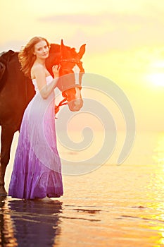 Beautiful woman riding a horse at sunset on the beach. Young girl with a horse in the rays of the sun by the sea.