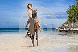 Beautiful woman riding a horse on tropical beach