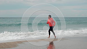 Beautiful woman is running in surf waves on empty sandy beach at stormy summer day. Happy carefree female on tropical beach runs a