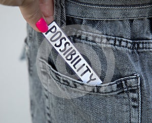 A beautiful woman`s hand with a bright manicure takes a paper with the inscription Possibility from the pocket of her jeans. Phot