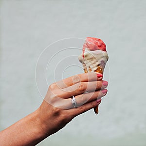 Beautiful woman's hand with a ring on her finger holding a colorful ice-cream cone. Close up. Outdoor.