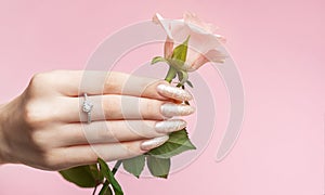 Beautiful woman's nails with pearl manicure and rose on pink background