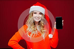 a beautiful woman in a Santa Claus hat with smartphone on a red background.