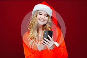 a beautiful woman in a Santa Claus hat with smartphone on a red background.