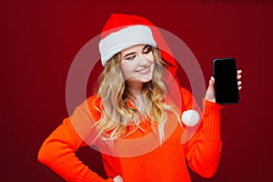 a beautiful woman in a Santa Claus hat with smartphone on a red background.