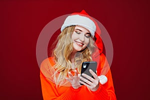 a beautiful woman in a Santa Claus hat with smartphone on a red background.