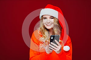 a beautiful woman in a Santa Claus hat with smartphone on a red background.