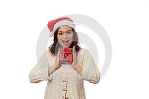 Beautiful woman in Santa hat, holding Christmas present and expressing happiness and positive emotions looking at camera