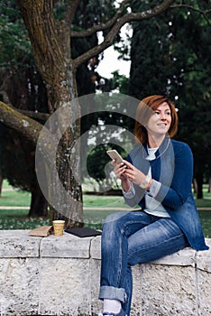 Beautiful woman sending a message on her phone in the park