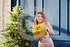 a beautiful woman in a shiny dress with a gift by the christmas tree.