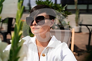 Beautiful woman with short brunette hair in white clothes and sunglasses. Fashion photography. Fashion model posing with