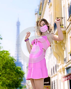 Beautiful woman in short light slim pink summer dress and medical mask Eiffel Tower in Paris