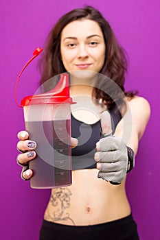 Beautiful woman showing a protein shaker with thumbs up gesture.