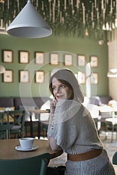 Beautiful woman sit in cafe, looking in window. Girl at round table in cafe. Vertical frame