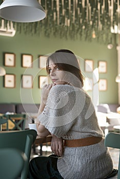 Beautiful woman sit in cafe, looking in window and thinking about something. Girl at round table in cafe. Vertical frame