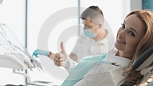 A beautiful woman sits comfortably in a dental chair and with an approving hand gesture recommends a dental clinic that