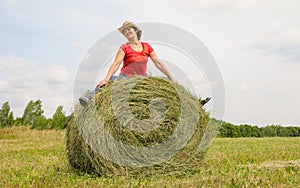 Beautiful woman sits on a hay in a field