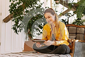 A beautiful woman sits at home among a large number of plants and communicates with relatives or friends using a tablet