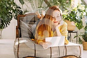 A beautiful woman sits at home among a large number of plants and communicates with relatives or friends using a tablet