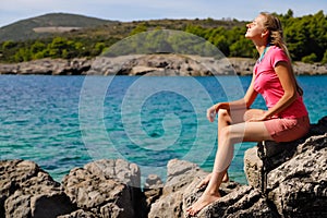 Beautiful woman sits on rock against the azure sea and breathes fresh air on vacation