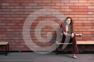 Beautiful woman sitting on a bench on a brick wall background