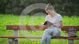 Beautiful Woman sitting on a bench in the park and reading a book, Student preparing for the exam in the garden, young