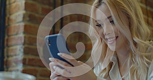 Beautiful woman sitting at a cafe using mobile phone and smiling. Female reading text message on her smart phone at a