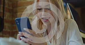 Beautiful woman sitting at a cafe using mobile phone and smiling. Female reading text message on her smart phone at a