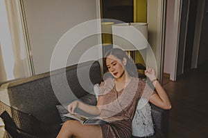 A beautiful woman sitting on the cozy sofa, reading magazine