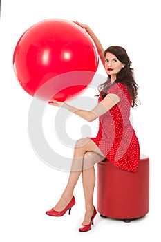 Beautiful woman sitting on footstool holding big red balloon