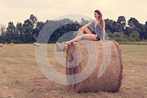 Beautiful woman sitting on hay bale a summer`s day
